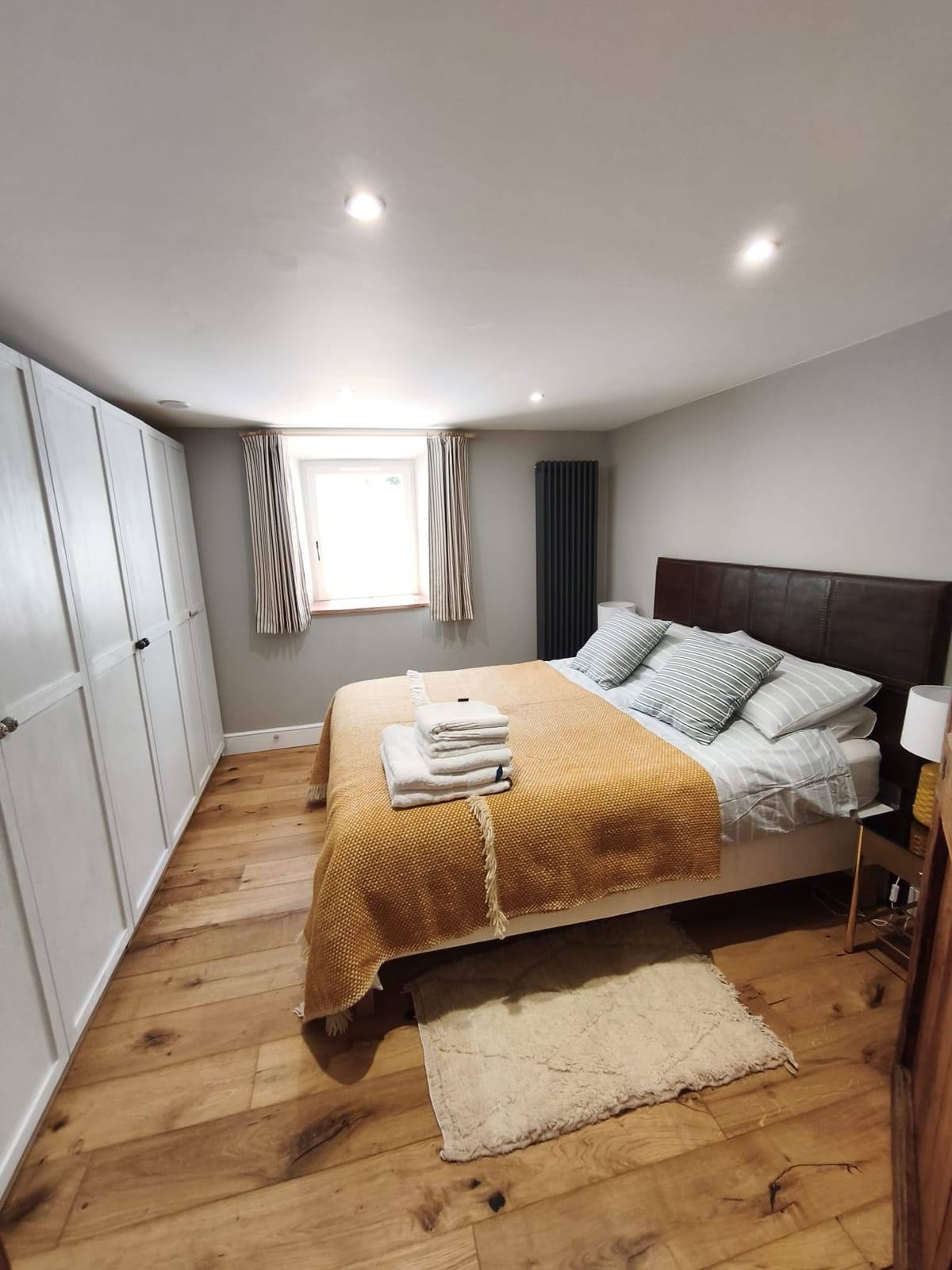 La même pièce après rénovation, devenue une chambre : parquet en chêne, placards intégrés blancs, radiateur vertical et fenêtre habillée de rideaux