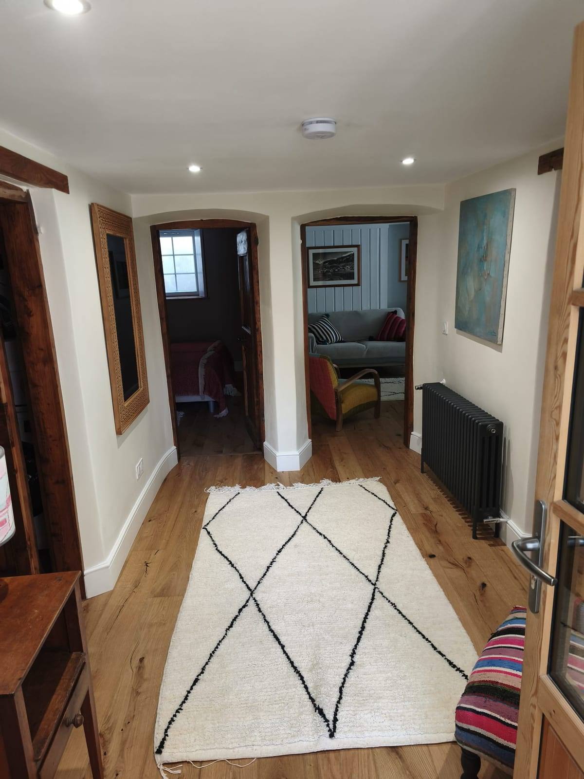 Le même passage après rénovation : parquet en chêne massif, arcades habillées de bois, murs blancs, spots encastrés et radiateur en fonte