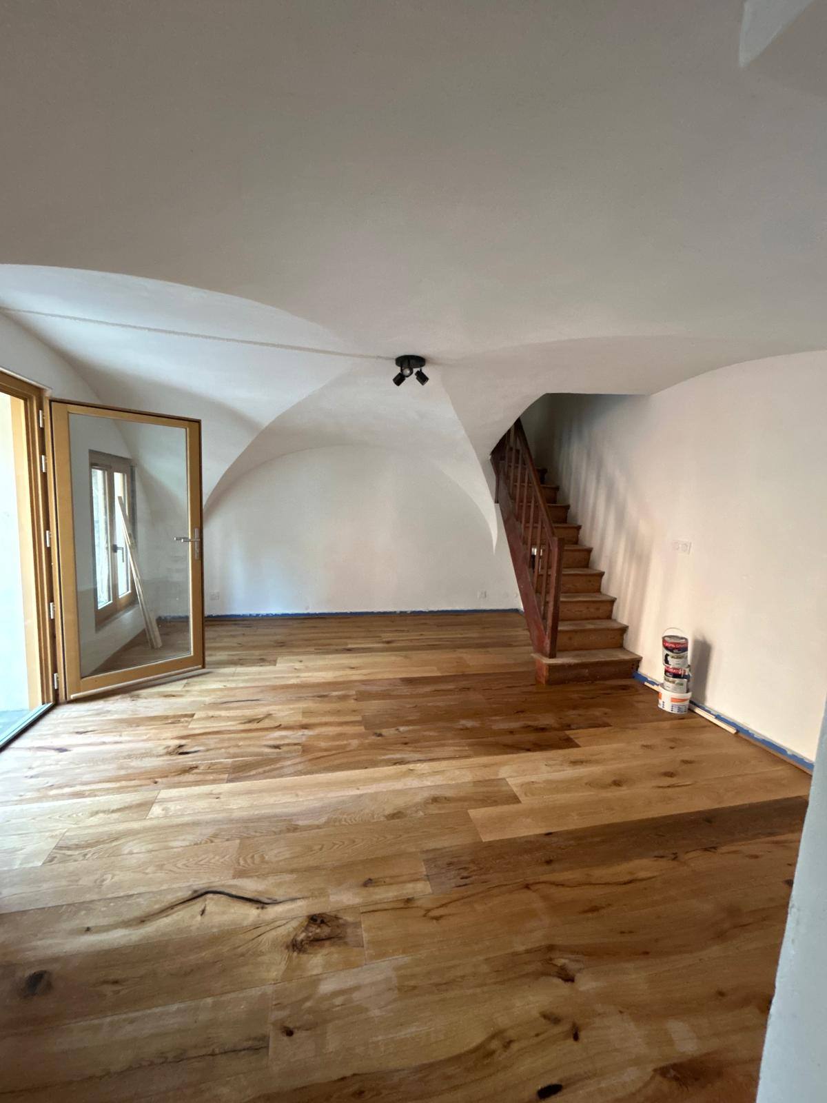 La même pièce de vie voûtée après rénovation : parquet en chêne massif, murs repeints en blanc et escalier bois mis en valeur
