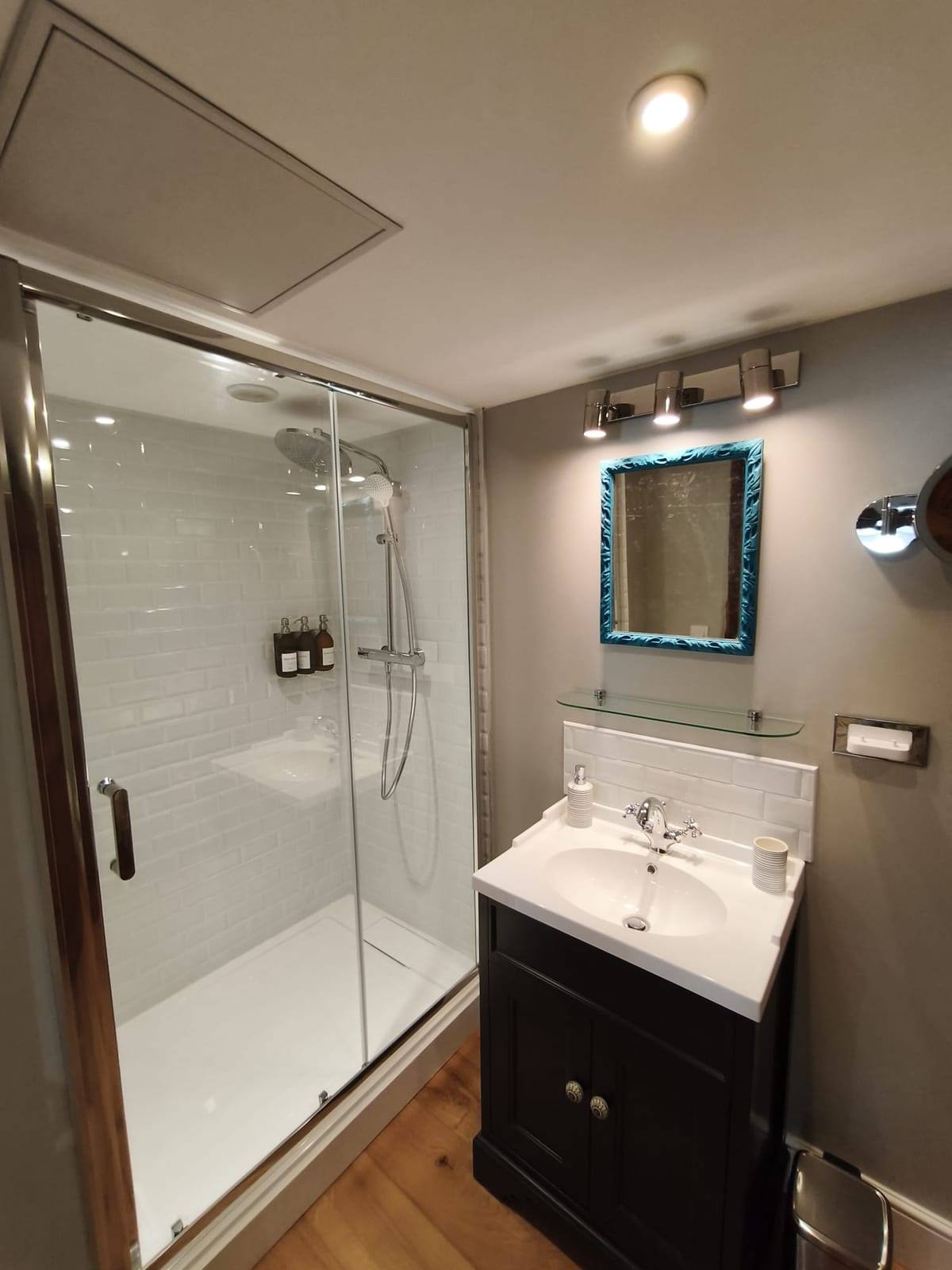 Salle d’eau rénovée avec cabine de douche vitrée, meuble vasque en bois foncé et miroir encadré