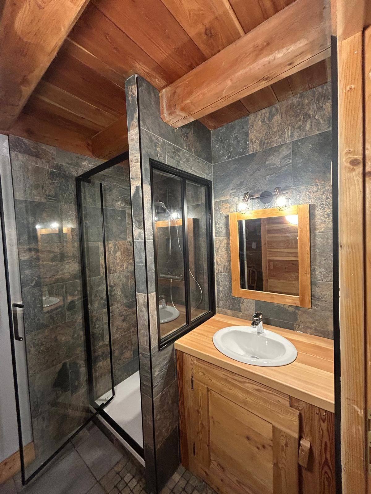 Salle de bain sous charpente avec faïence effet ardoise, cabine de douche vitrée et meuble vasque en bois massif