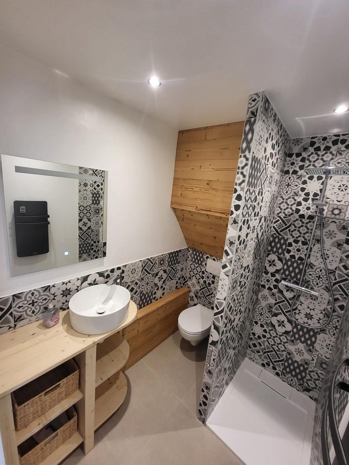 Salle de bain rénovée avec carreaux de ciment noir et blanc, douche à l’italienne et meuble vasque en bois